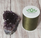 Amethyst next to spool of thread on wood grain background