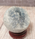 Blue Celestite Sphere on wood stand over wood grain in front of brick Gypsy Gems & Jewelry