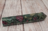 Ruby Fushite carved wand obelisk on wood grain background