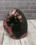 Rhodonite Freeform Tower Carved Gemstone Black and Pink on brick and wood grain background