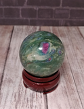Ruby Fushite carved sphere on brick and wood grain background