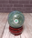 Ruby Fushite carved sphere on wood grain background