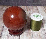 Red Jasper Sphere on wooden stand next to spool of thread size reference GGandJ.com