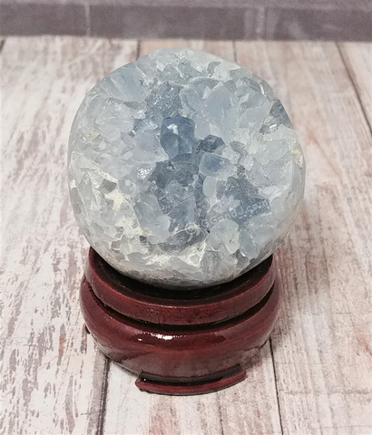 Blue Celestite Sphere on wood stand over wood grain in front of brick Gypsy Gems & Jewelry