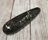 Natural black and pink gemstone wand on wood grain background Rhodonite
