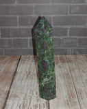Ruby Fushite carved wand obelisk on brick and wood grain background